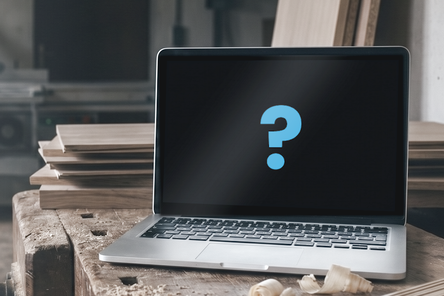 Ein Laptop steht auf einer alten Hobelbank in einer Tischlerei, daneben Hobelspäne und ein Stapel Holzplatten, im Hintergrund unscharf eine Formatkreissäge. Der Bildschirm ist schwarz, und in der Mitte steht ein blaues Fragezeichen — welches Programm es werden soll, ist offen