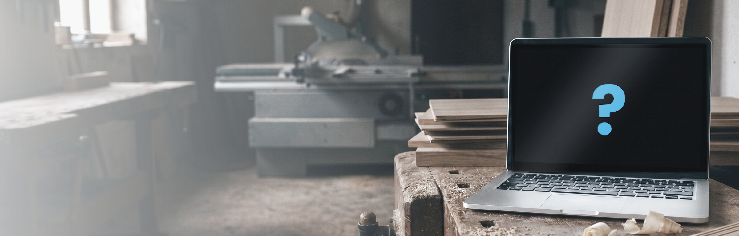 Ein Laptop steht auf einer alten Hobelbank in einer Tischlerei, daneben Hobelspäne und ein Stapel Holzplatten, im Hintergrund unscharf eine Formatkreissäge. Der Bildschirm ist schwarz, und in der Mitte steht ein blaues Fragezeichen — welches Programm es werden soll, ist offen