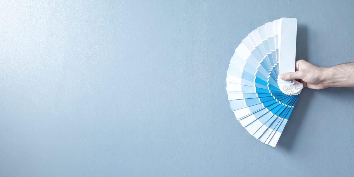 Hand hält einen Farbfächer an eine blau gestrichene Wand