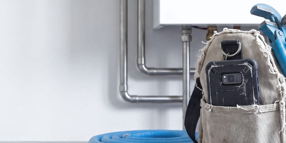 Werkzeugtasche mit Rohrzangen und Smartphone vor einer Heiztherme
