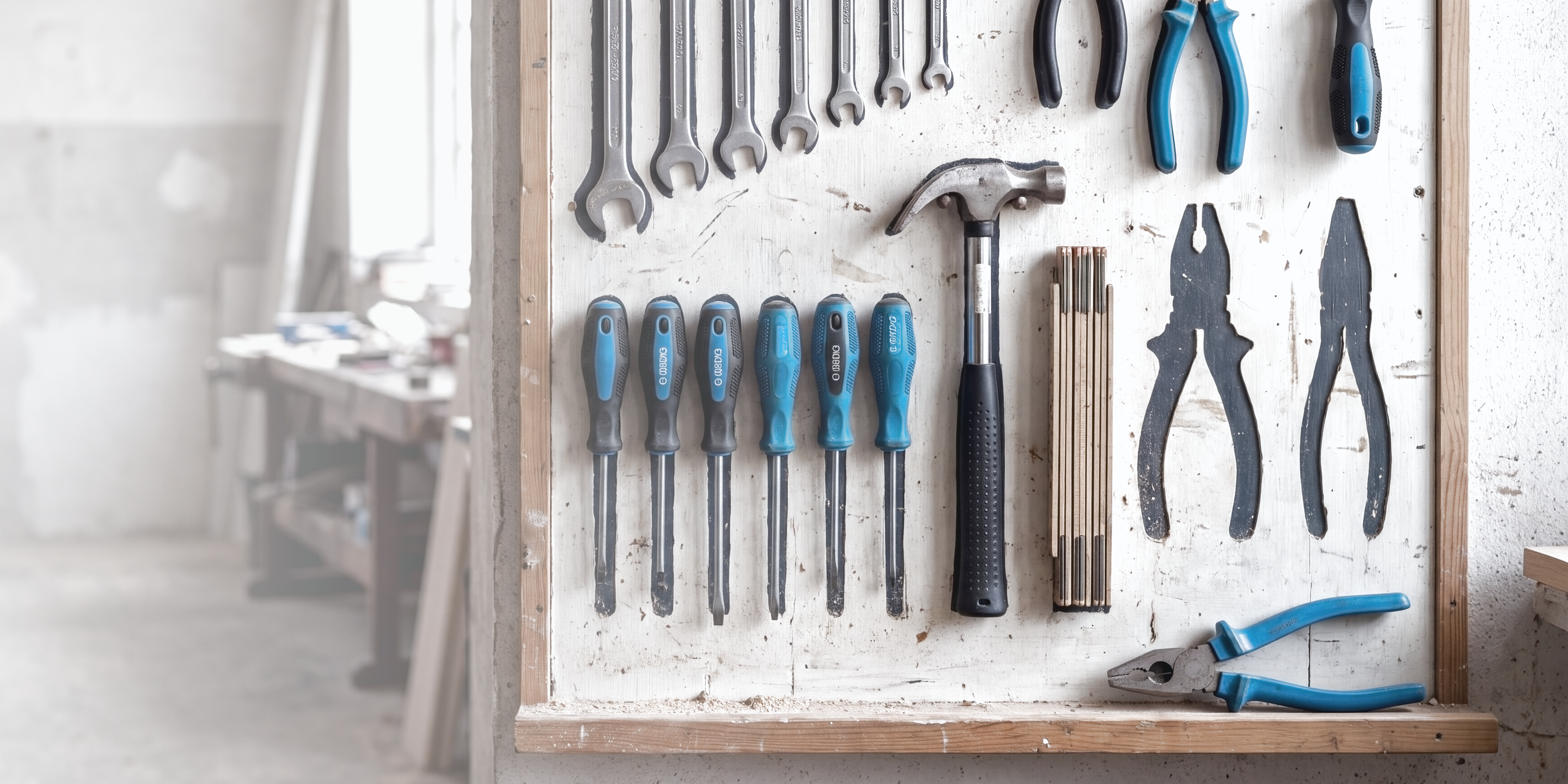 Foto einer Werkzeugwand in der Werkstatt: fast alle aufgemalten Umrisse sind mit dem passenden Werkzeug belegt, zwei Umrisse sind noch frei, die passende blaue Zange liegt auf der Ablage darunter